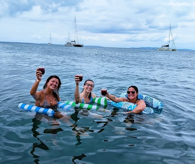 Friends in the water on floaties raising glasses of sangria