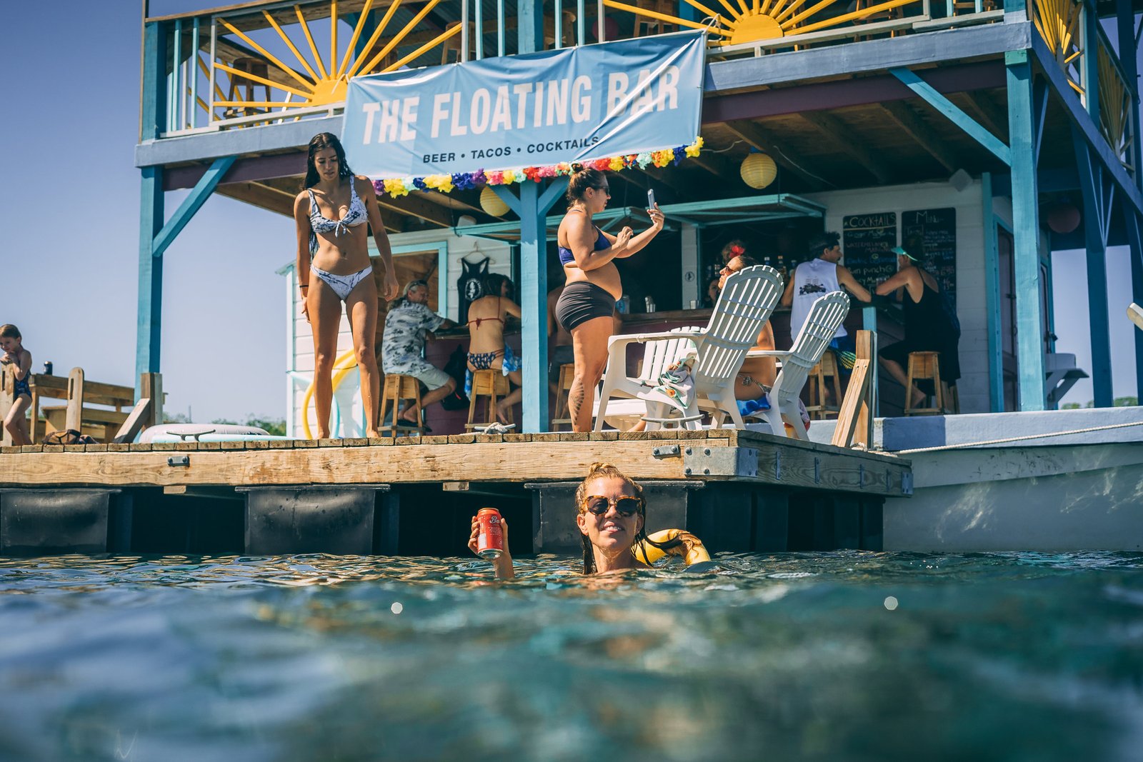 Guests on the swim deck and in the water with a drink at The Floating Bar