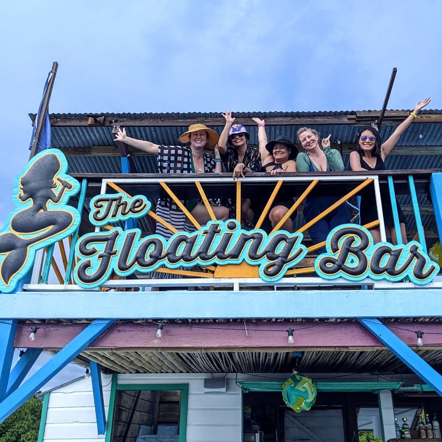 Friends waving from the top deck behind The Floating Bar sign