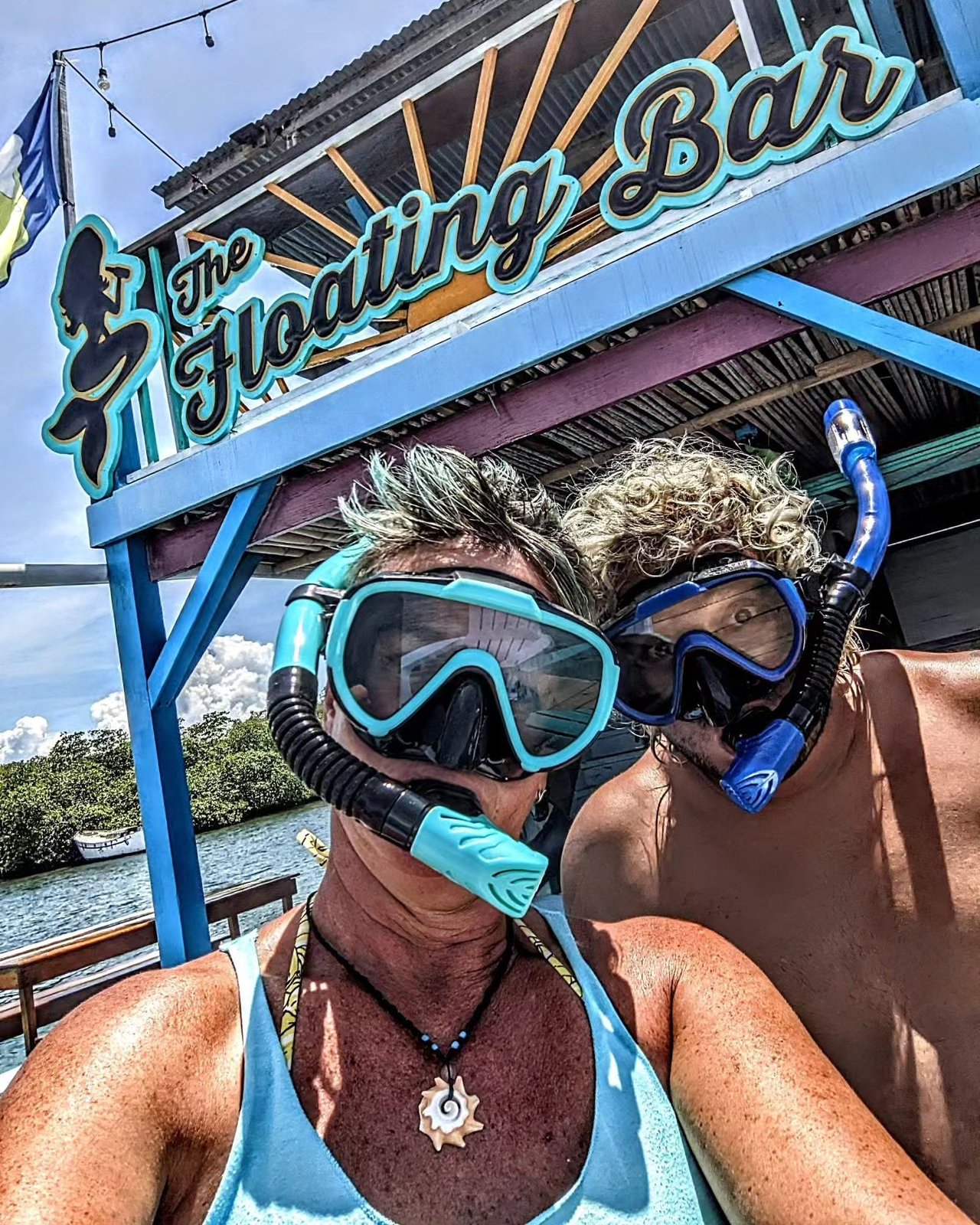 Two snorkelers in masks under The Floating Bar sign, ready to explore the wreck next door